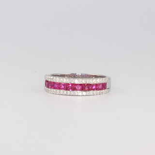 A white metal stamped 750 Art Deco style ruby and diamond cocktail ring with 11 princess cut rubies (3 chipped), flanked by brilliant cut diamonds, the rubies 1.09ct, the diamonds 0.3ct, size O 1/2, 4.2 grams 