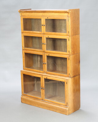 A light oak 4 tier Minty style bookcase enclosed by panelled doors 141cm h x 89cm w x 28cm d  