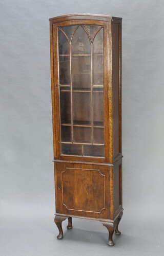A 1930's Art Deco arch shaped oak display cabinet, fitted shelves enclosed by arched panelled glazed door, the base enclosed by panelled doors, raised on cabriole supports 170cm h x 47cm w x 17cm d (cabinet is locked and is missing 2 escutcheons, 1 glass panel cracked) 
