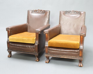 A pair of 1920's carved oak armchairs upholstered in brown material with loose cushions, raised on cabriole supports 80cm h x 64cm w x 70cm d 