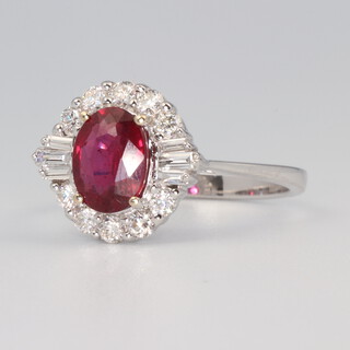 A white metal stamped 750 oval ruby and diamond cluster ring, the centre stone approx. 1.45ct, the tapered baguette diamonds 0.12ct, the brilliant cut diamonds 0.37ct, 3.5 grams, size N 1/2
