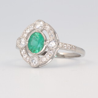 A white metal stamped plat Art Deco style emerald and diamond cluster ring, the oval cut emerald 0.80ct, the brilliant cut diamonds 0.30ct, 4 grams, size N 