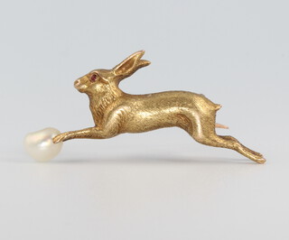 A yellow metal bar brooch in the form of a hare with a ruby eye chasing a baroque pearl 4.5 grams, 30mm 