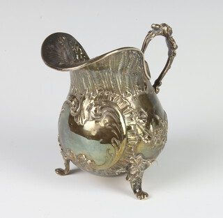 A 19th Century Continental repousse silver cream jug with vacant cartouche raised on scroll legs, London import marks 1891, 94 grams, 9cm 