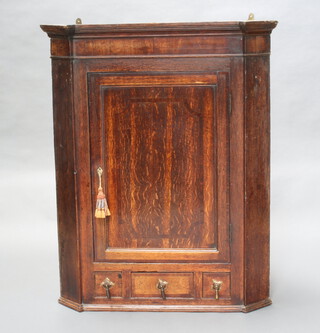 A Georgian oak hanging corner cabinet with moulded cornice, fitted shelves enclosed by a panelled door, the base fitted 1 long and 2 dummy drawers 107cm h x 85cm w x 54cm d 
