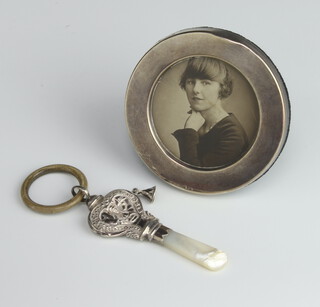 A circular silver photograph frame Sheffield 1980 9.5cm (dented) together with a repousse silver childs rattle teether (1 rattle missing) Birmingham 1924 