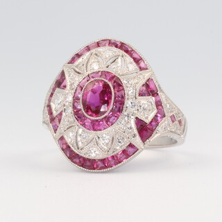 A white metal ruby and diamond cocktail ring, the centre oval cut ruby surrounded by tapered cut rubies approx. 1.15ct and brilliant cut diamonds approx. 0.7ct, size M 1/2, 5.4 grams 
