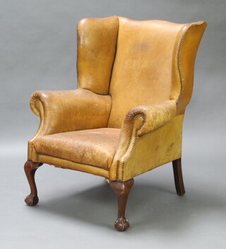 A Georgian style winged armchair upholstered in brown leather, raised on cabriole ball and claw supports 112cm h x 90cm w x 73cm d (staining to the seat)