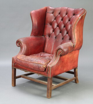 A Georgian style winged armchair upholstered in red button back leather raised on square supports with double H frame stretcher (chair is in barn condition, tear to the left arm, cushion is worn) 110cm h x 87cm w x 66cm d (seat 38cm x 46cm) 