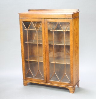 A 1930's oak display cabinet with raised back, fitted shelves enclosed by astragal glazed panelled doors, raised on bun feet 127cm h x 93cm w x 30cm d 