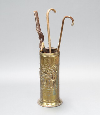 An embossed brass stick stand decorated a tavern scene 55cm h x 20cm diam. containing 3 sticks, a riding crop and a whip 