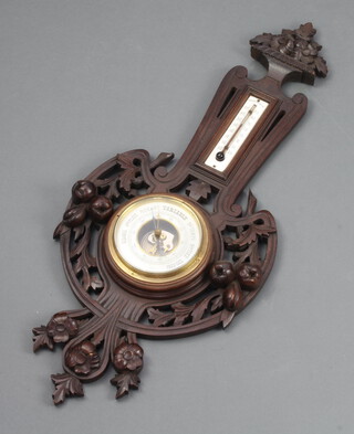 A French Edwardian aneroid barometer and thermometer with silvered dial, contained in a carved and pierced walnut wheel case decorated fruit 69cm x 28cm 