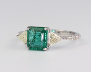 A white metal stamped 18ct emerald and diamond ring, the centre emerald approx. 1.65ct, the triangular diamonds 0.57ct, 3 grams, size M 1/2