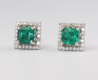 A pair of white metal stamped 18ct princess cut emerald and diamond ear studs, the centre stones 1.72ct and the diamonds 0.35ct, 8mm x 8mm, 4.2 grams 