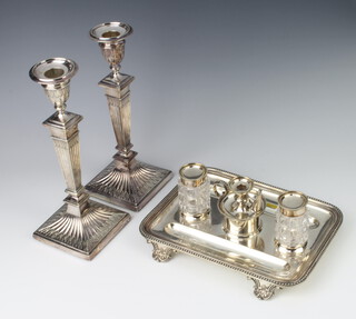 A silver plated ink stand with cut glass mounted bottles and a central chamber stick, raised on scroll feet with presentation inscription, a pair of tapered candlesticks 