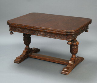 A carved oak draw leaf dining table, the apron carved grapes, raised on cup and cover supports with H framed stretcher 77cm h x 127cm l x 91cm w