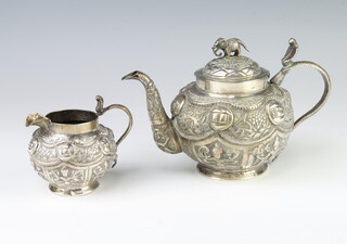 An Indian white metal baluster teapot decorated with figures having an elephant finial, 688gms with matching cream jug 