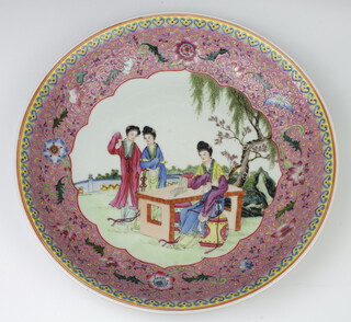 A 20th Century Chinese Republic style famille rose shallow dish decorated with figures at a table in a garden enclosed in a floral border 33cm 