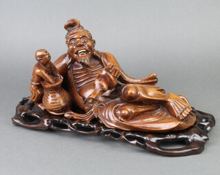 A carved Eastern figure of a reclining deity raised on a pink marble stand 20cm h x 40cm w x 22cm d 