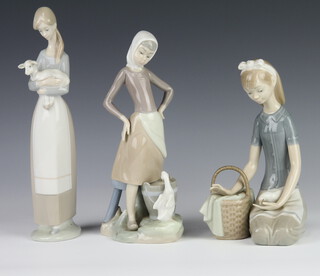 A Lladro figure of a girl holding a lamb 26cm, a ditto of a goose girl with pail 23cm and a kneeling girl with dove 20cm 
