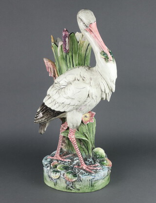 In the manner of Joseph Holdcroft, a 19th Century Majolica figure of a standing stork with a frog it its mouth standing beside a cluster of bull rushes, raised on a round base with lily pads, the underside stamped 7820 and 4, 60cm 