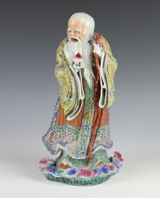 A 19th Century Chinese porcelain figure of a standing Shoulao holding a peach in his right hand, a staff in his left, raised on a base of polychrome waves 35cm 
