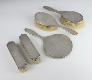 A 5 piece engine turned silver backed dressing table set comprising hand mirror, 2 clothes brushes, 2 hair brushes with vacant cartouche, Birmingham 1931 and 32