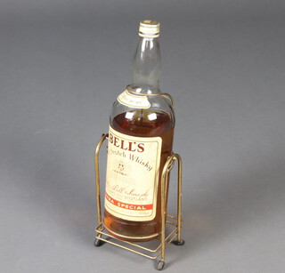 A 4.5 litre bottle of Bells Old Scotch Whisky contained in a metal cradle, the seal to the bottle has been broken and opened, the contents is down to the top of the label  
