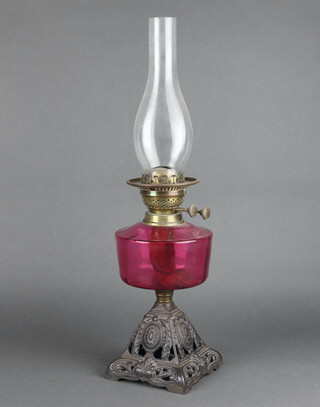 A Victorian cranberry glass oil lamp reservoir raised on a square pierced cast iron base, complete with clear glass chimney 56cm h x 15cm w x 16cm d 