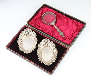 A pair of Edwardian pierced and repousse silver bon bon dishes Sheffield 1902, 56 grams, 12cm, in a fitted case, together with a silver handled magnifying glass 