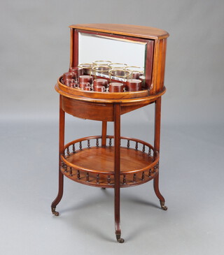 Albert Baker, an Edwardian mahogany circular 2 tier drinks table, the upper section having a mirrored panelled door revealing a revolving cabinet, the base with bobbin turned decoration, raised on outswept supports, marked Albert Baker Ltd, 5 New Bond Street, London 98cm h x 55cm w x 49cm d 