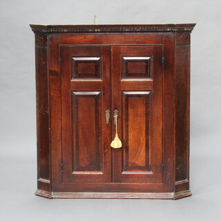 A Georgian oak hanging corner cabinet with moulded and dentil cornice enclosed by panelled doors complete with polished key 105cm h x 97cm w x 64cm d 