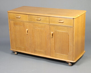 An Ercol light elm sideboard fitted 3 drawers above triple cupboard, raised on casters 76cm h x 131cm w x 49cm d 