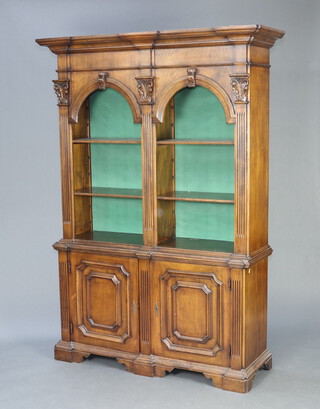 A Continental walnut bookcase on cabinet, the upper section with moulded cornice, fitted a pair of arch shaped bookcases with adjustable shelves, the base enclosed by a panelled door, raised on square supports 217cm h x 154cm w x 47cm d 

