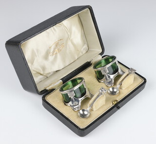 An Edwardian Art Nouveau silver condiment set comprising 2 salts with green glass liners and 2 spoons, Birmingham 1906