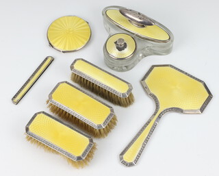 A silver and yellow guilloche enamel dressing table set comprising hand mirror, 2 clothes brushes, hair brush, comb mount, nail buffer, compact (a/f) and lidded glass base (a/f), Birmingham 1927 and 1928 