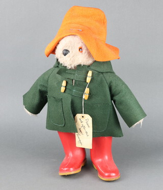 A Paddington Bear with orange hat and green duffle coat, complete with label and red Dunlop wellingtons 