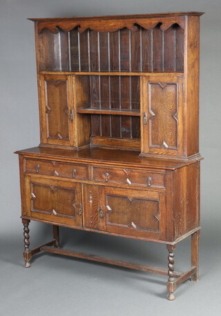 A 1920's Jacobean style oak dresser the raised back with moulded cornice, shelf above recess flanked by pair of cupboards, the base fitted 2 drawers with drop handles, raised on spiral turned supports, H framed stretcher 191cm h x 138cm w x 46cm d  