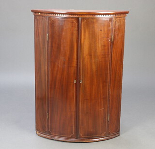 A Georgian inlaid mahogany bow front hanging corner cabinet with moulded and dentil cornice, the interior fitted shelves enclosed by panelled doors 98cm h x 70cm w x 48cm d 