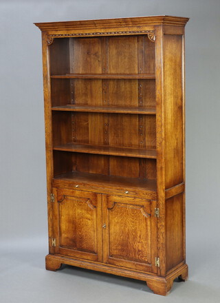 An Ipswich style carved oak bookcase with moulded cornice and adjustable shelves, the base fitted a brushing slide above cupboard enclosed by arch panelled doors, raised on bracket feet 199cm h x 116cm w x 40cm d 