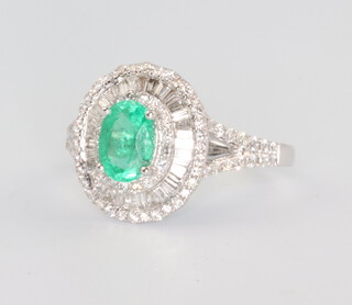 A 14ct white gold oval emerald and diamond cluster ring, the centre stone 0.85ct, the brilliant and tapered baguette diamonds 0.9ct, 3.2 grams, size N 1/2