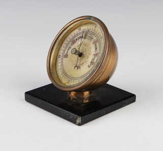 A 1930's aneroid desk barometer with 7cm circular silvered dial contained in a gilt metal case and raised on a black onyx base 8cm x 8cm x 8cm 