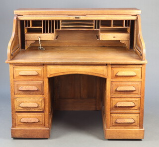 A 19th/20th Century oak roll top kneehole pedestal desk with tambour shutting revealing a well fitted interior, the base with 1 long drawer flanked by brushing slides above 8 short drawers 122cm h x 126cm w x 82cm d  