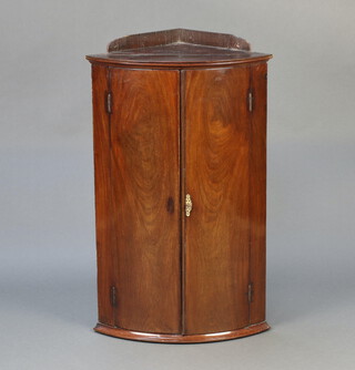 A Georgian mahogany bow front hanging corner cabinet with raised back, fitted shelves enclosed by panelled doors 97cm h x 59cm w x 40cm d 