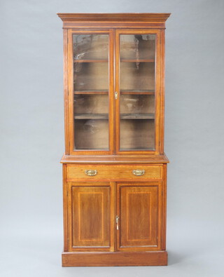 An Edwardian inlaid mahogany bookcase on cabinet with moulded cornice, fitted shelves enclosed by glazed panelled doors, the base fitted a drawer above double cupboard enclosed by panelled doors, raised on a platform base 210cm h x 89cm w x 41cm d 