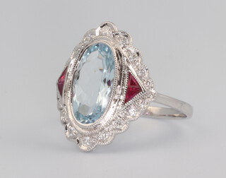 A white metal stamped 18k ring set with an oval aquamarine, flanked by rubies and surrounded by brilliant cut diamonds, the aquamarine 2.19ct, rubies 0.09ct, diamonds 0.16ct, size J, 3.1 grams 