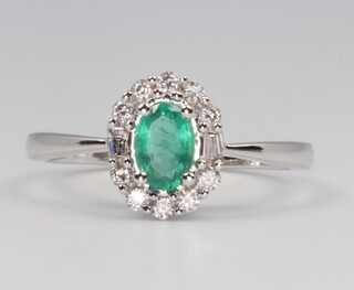 A white gold stamped 18k oval emerald and diamond cluster ring, the central emeral a0.45ct the diamonds 0.25ct, with original WGI certificate no, WG19624126538, size N, 2.8 grams