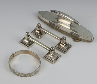 A pair of Victorian silver knife rests London 1896, an oval silver nail buffer and a silver bangle 