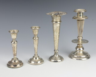 A pair of silver candlesticks raised on circular spreading feet Birmingham 1926 13cm h, a silver trumpet shaped vase with loaded base 19cm h and a Continental white metal candlestick 19cm h 