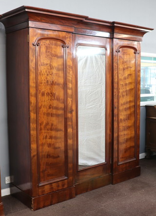 A Victorian triple inverted breakfront wardrobe with moulded cornice, the centre section fitted 4 shallow trays above 2 drawers with brass swan neck handles enclosed by arched plate panelled door, flanked by cupboards with hanging space above 1 long drawer 220cm h x 205cm w x 74cm d 